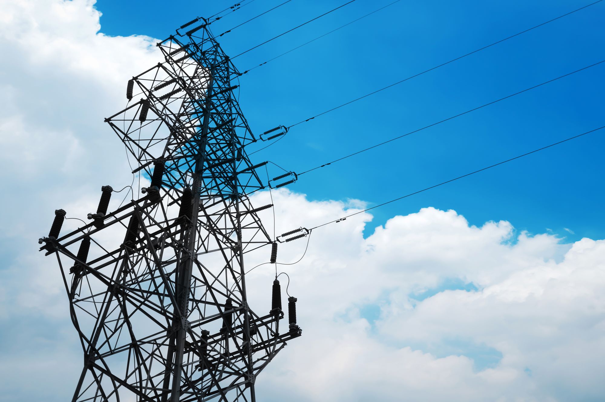 High-voltage power lines tower against a bright blue sky, showcasing the essential infrastructure for electricity transmission.